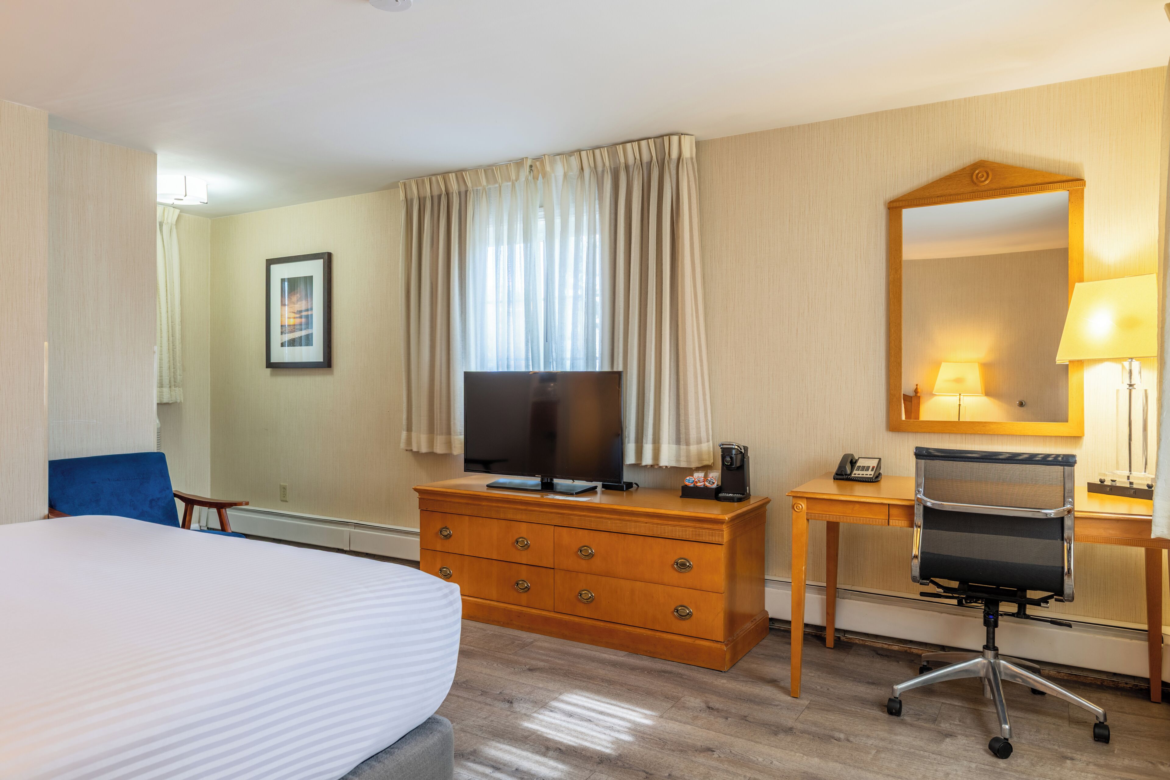 A hotel room with a bed, a desk with a chair, a TV, and a mirror.