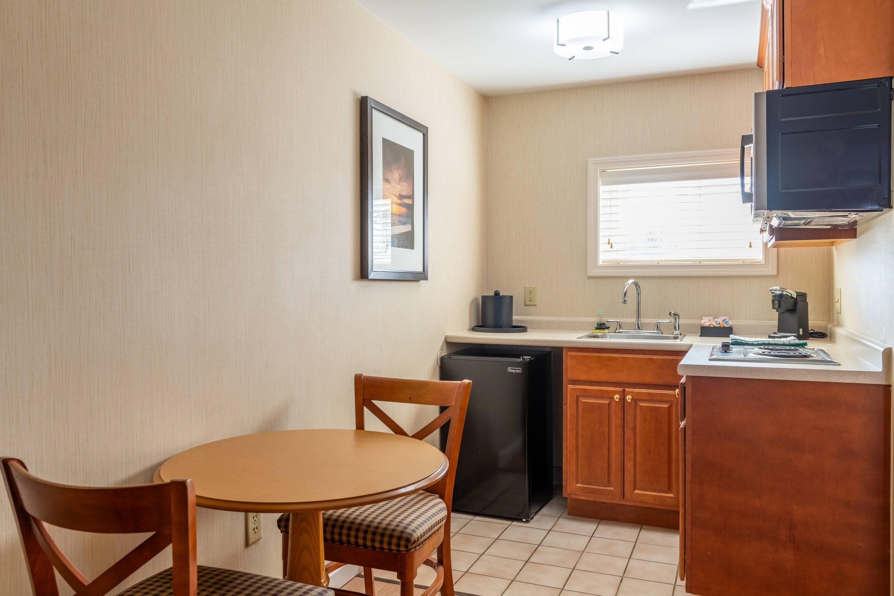 A compact kitchen with a dining table, chairs, a refrigerator, and a window with blinds.