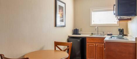 A compact kitchen with a dining table, chairs, a refrigerator, and a window with blinds.