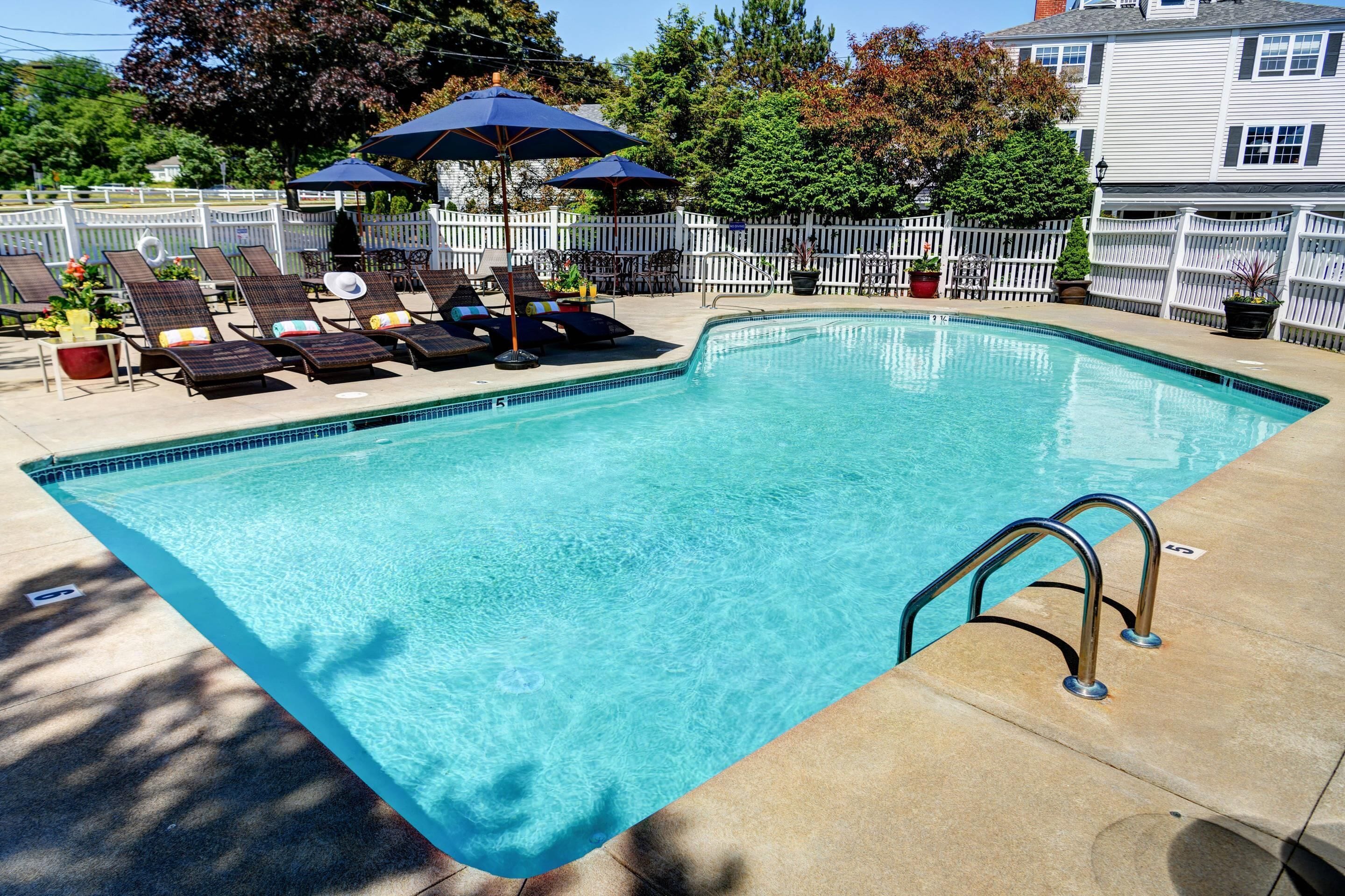 A rectangular swimming pool with a tiled edge, surrounded by a white fence.