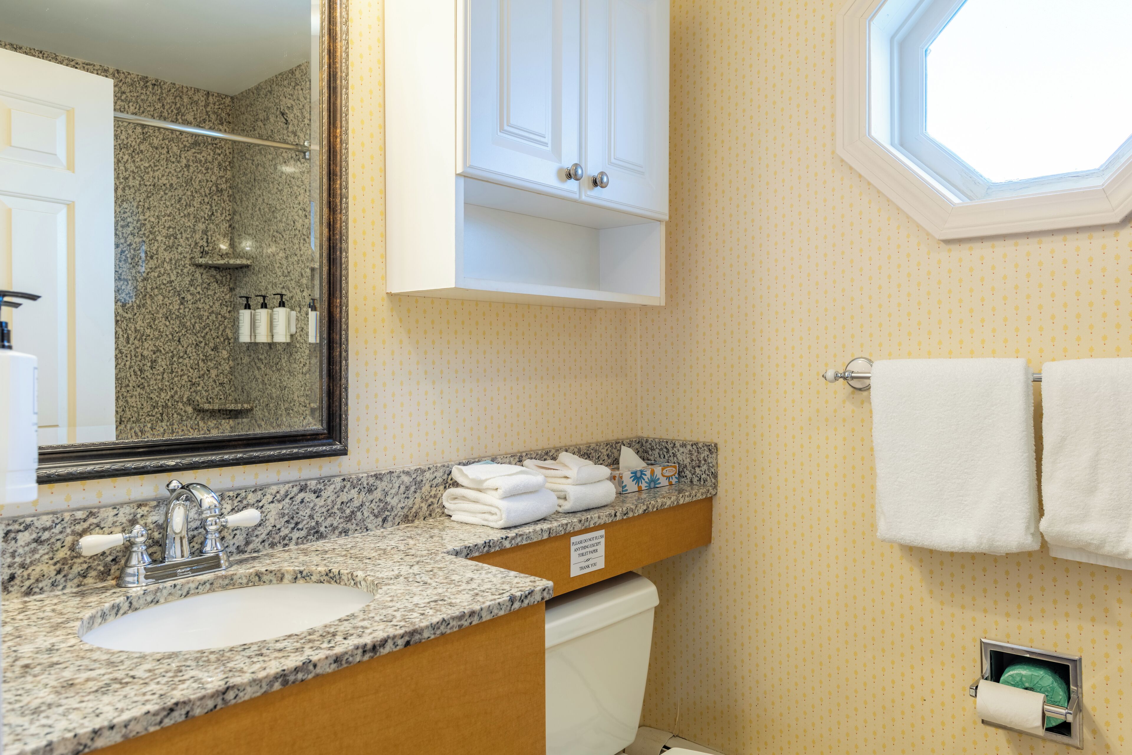 Un baño con lavamanos de encimera de granito, un espejo, toallero y una ducha visible al fondo.