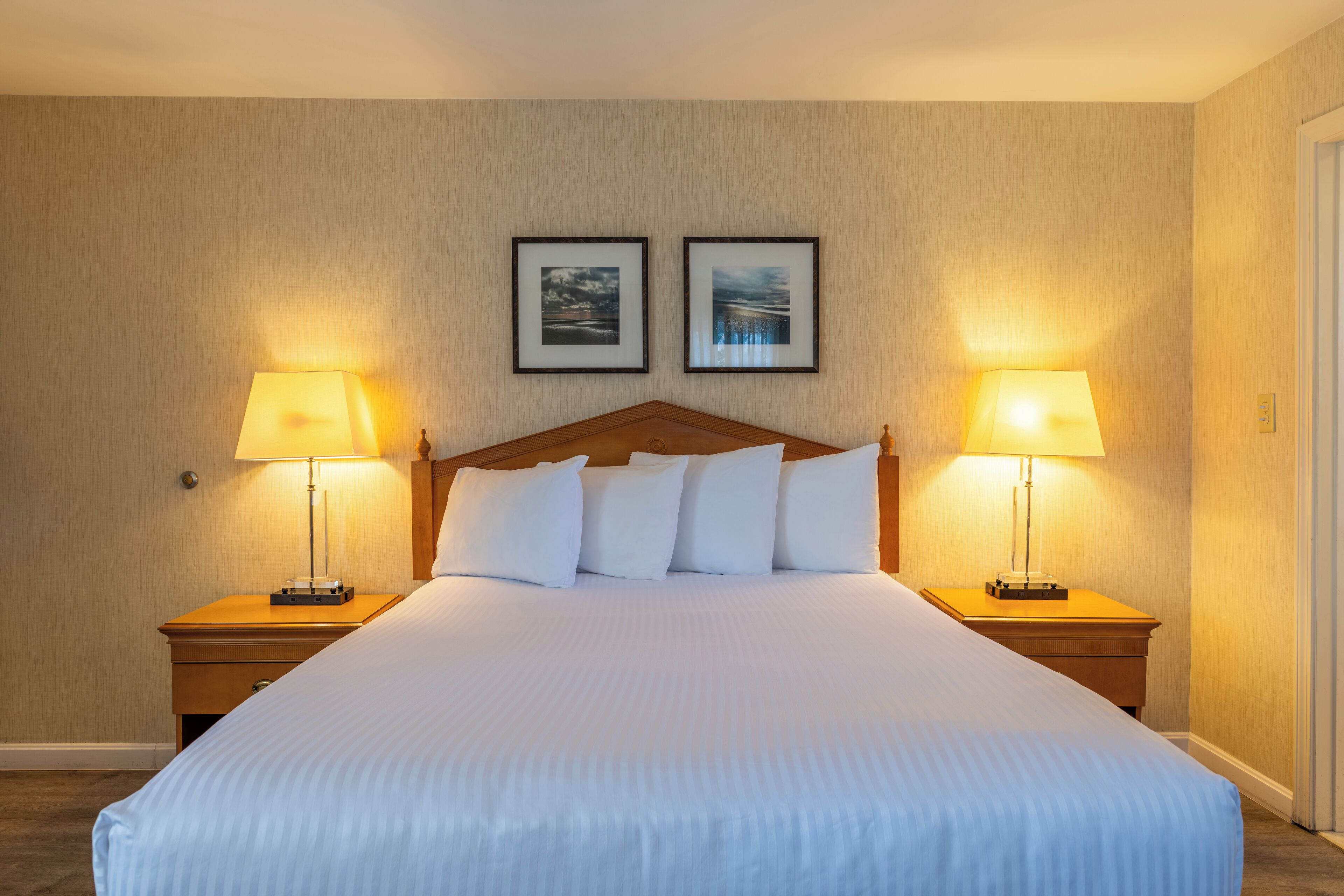 Una habitación de hotel con una cama grande, dos lámparas de noche y dos cuadros en la pared.