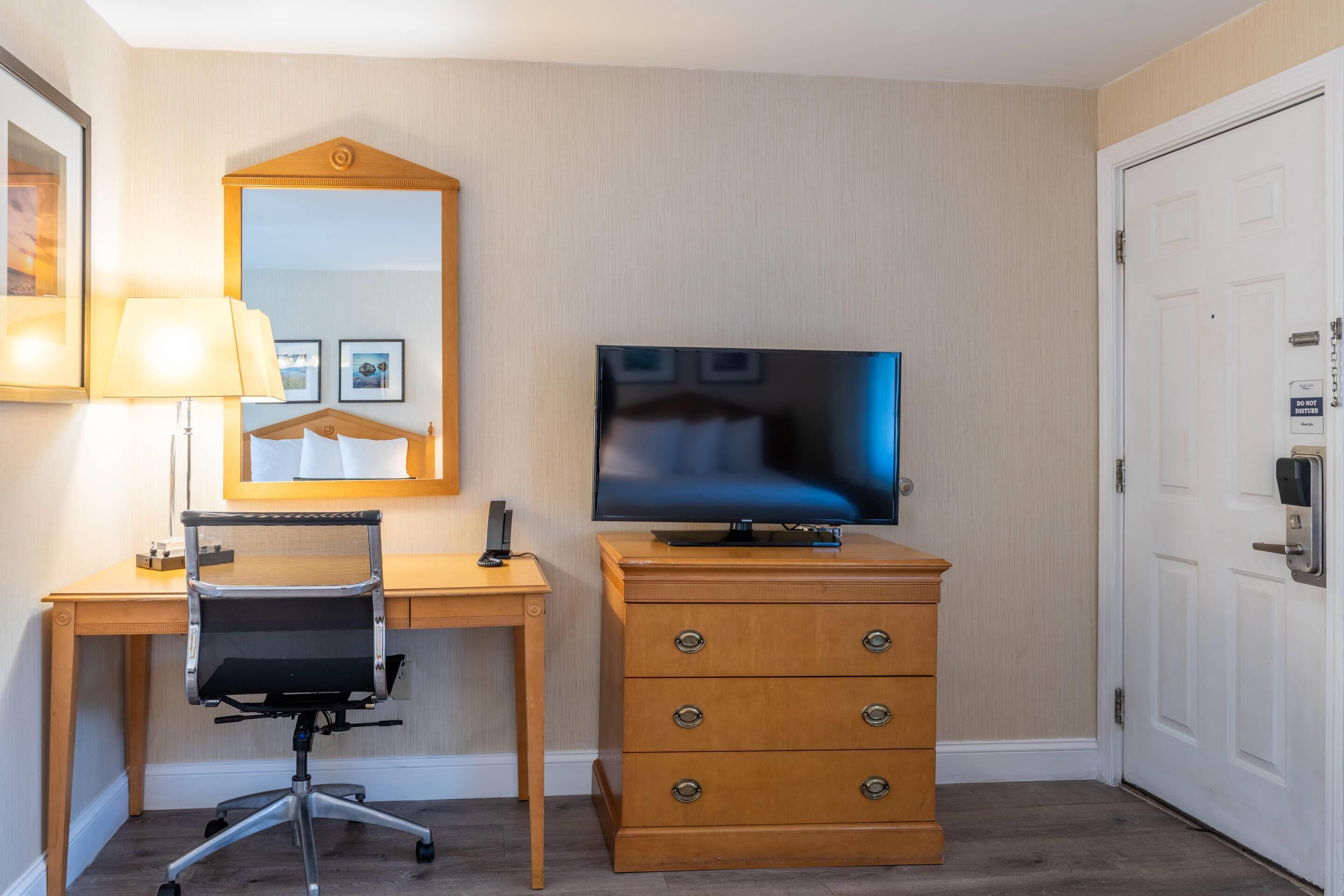 Habitación de hotel con un escritorio de madera, una silla, un televisor, un aparador y una puerta.