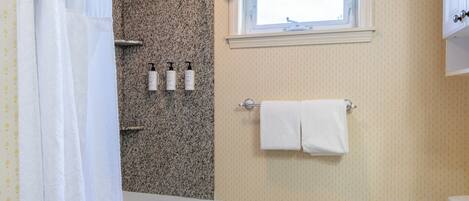 A bathroom with a bathtub, a window with a curtain, a towel rack with towels, and toiletries on the wall.