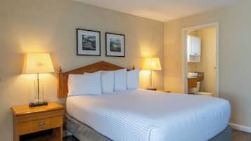 A hotel room with a large bed, two bedside lamps, a wooden nightstand, and a framed picture on the wall.
