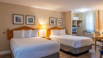 Une chambre d’hôtel avec deux lits, un bureau, une chaise, une lampe et des tableaux encadrés au mur.