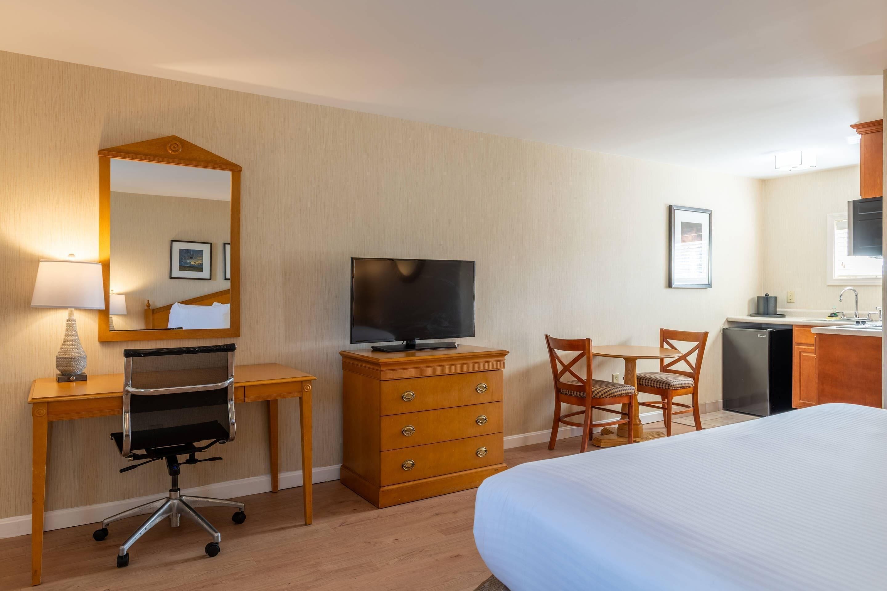 Ett hotellrum med en säng, skrivbord, stol, byrå, tv och ett litet pentry.