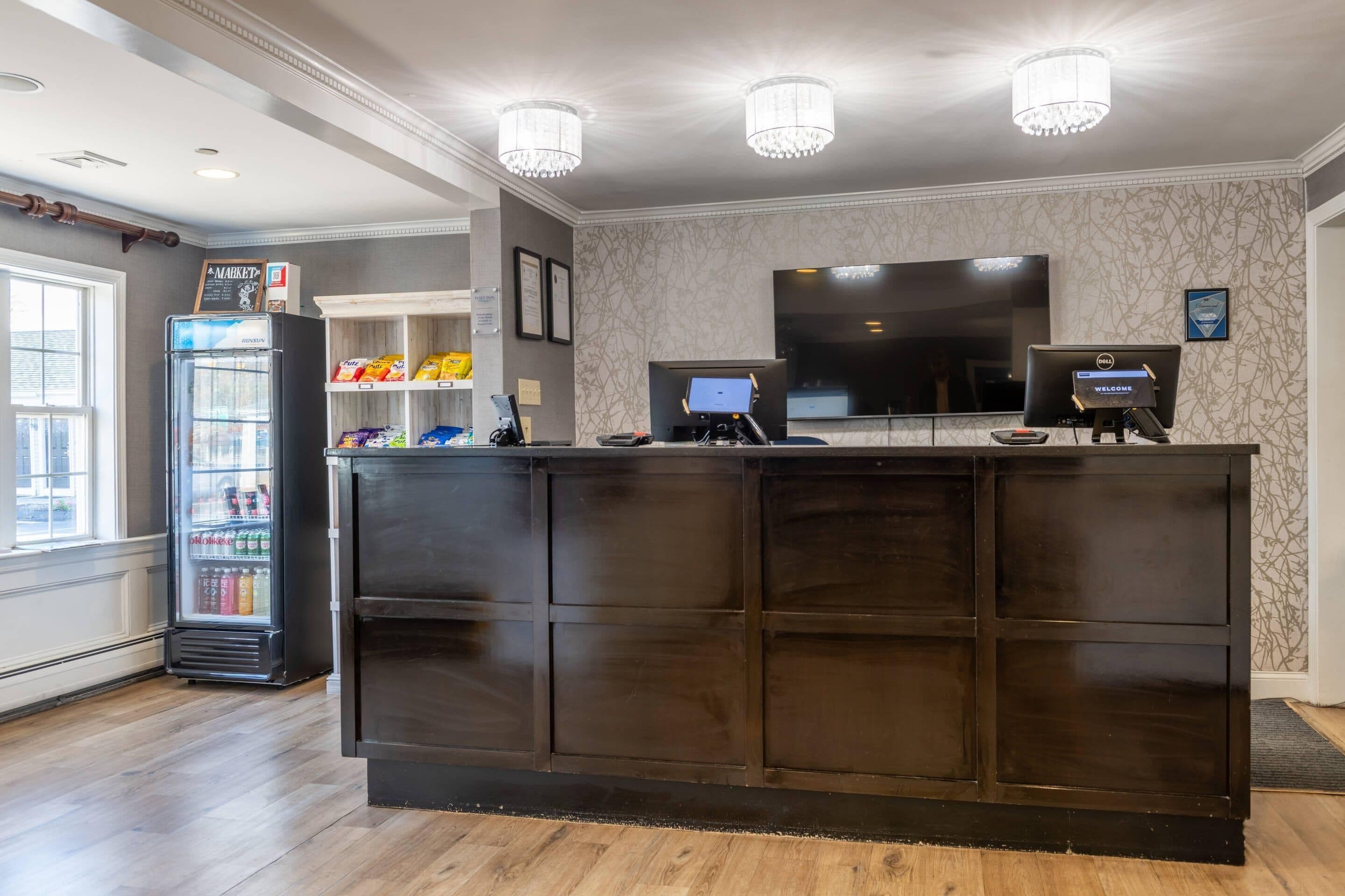 A reception desk with a dark wood finish, a refrigerator stocked with beverages, a flat-screen TV, and a digital kiosk.