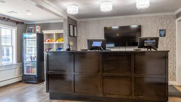 A reception desk with a dark wood finish, a refrigerator stocked with beverages, a flat-screen TV, and a digital kiosk.