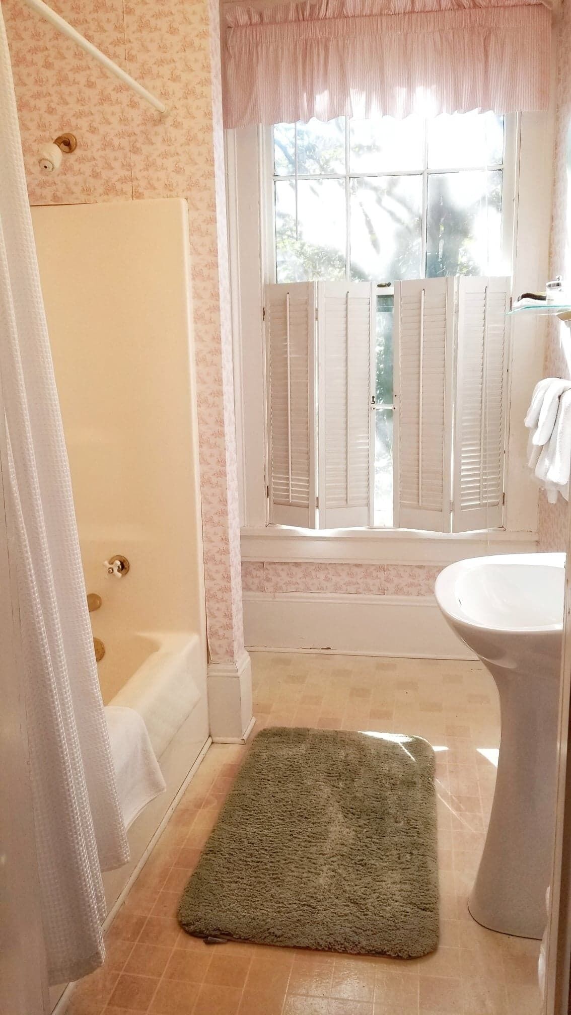 Un baño con ducha, una ventana con persianas, un lavabo y una alfombra verde en el suelo.