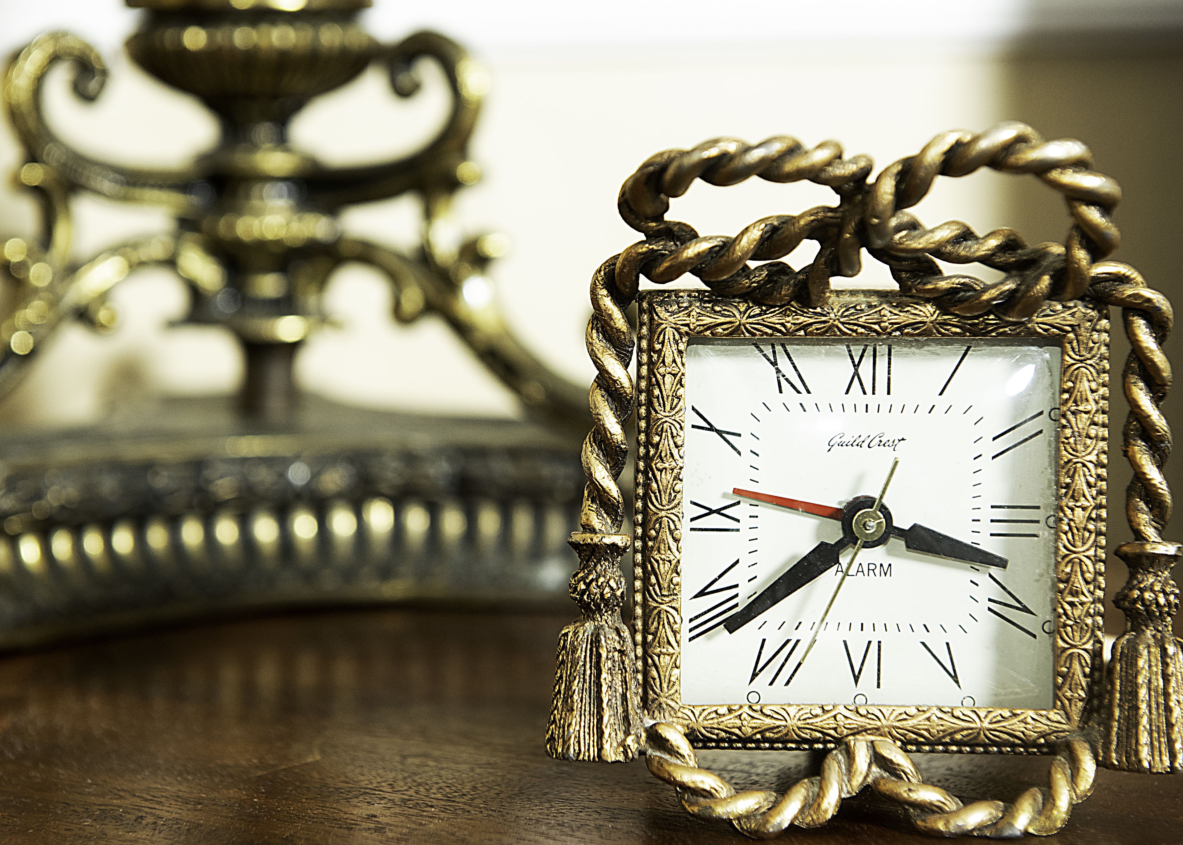 A gold-framed clock with Roman numerals and a red second hand, placed on a wooden surface.