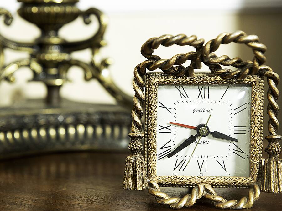 A gold-framed clock with Roman numerals and a red second hand, placed on a wooden surface.
