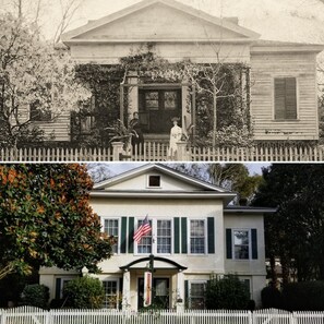 A two-story house with a white picket fence, a front porch, and a small flag.
