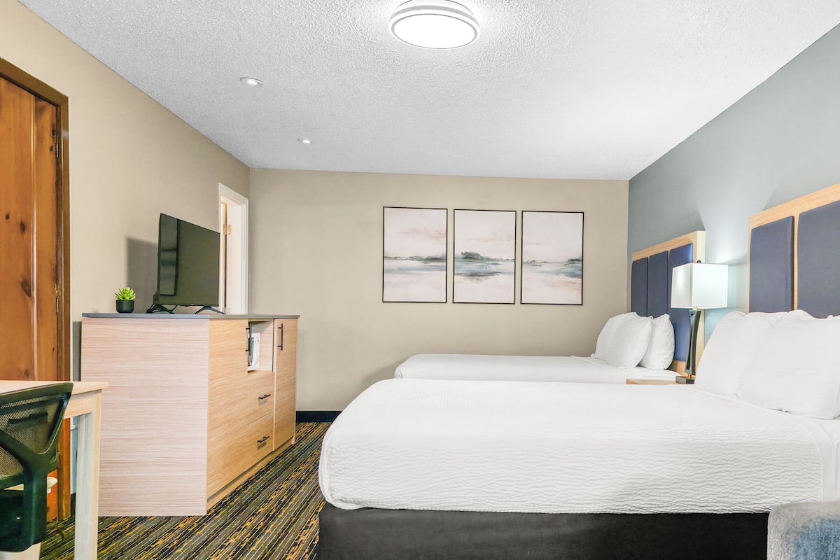 A hotel room with two beds, a wooden dresser, a television, and three framed pictures on the wall.