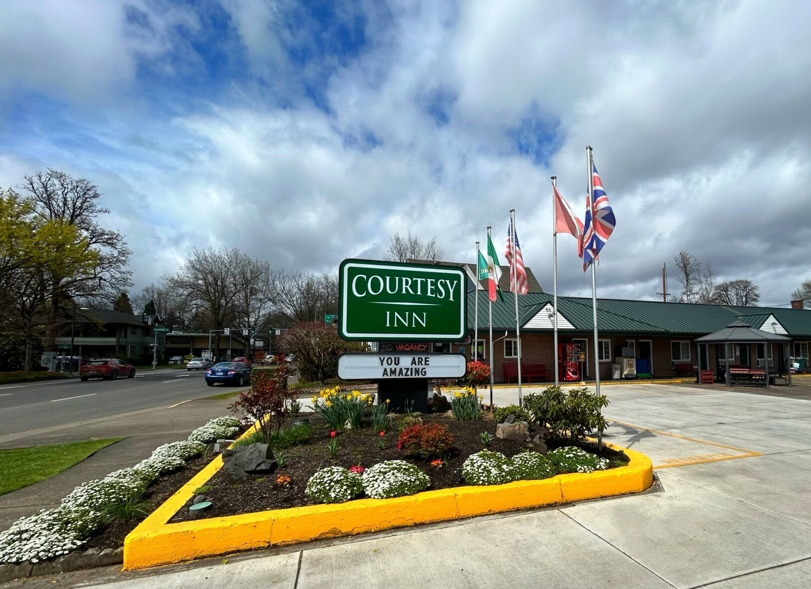 Une enseigne  « Courtesy Inn » avec des drapeaux, un parking et un bâtiment doté d’un toit végétalisé.