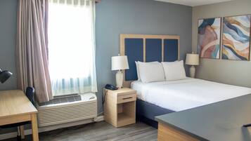 Habitación de hotel con cama, mesitas de noche, escritorio, silla, equipo de aire acondicionado y ventana con cortinas.