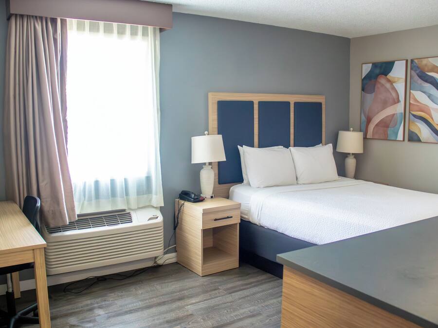 Habitación de hotel con cama, mesitas de noche, escritorio, silla, equipo de aire acondicionado y ventana con cortinas.