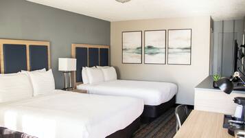 A hotel room with two beds, a desk, a chair, a lamp, and three framed pictures on the wall.