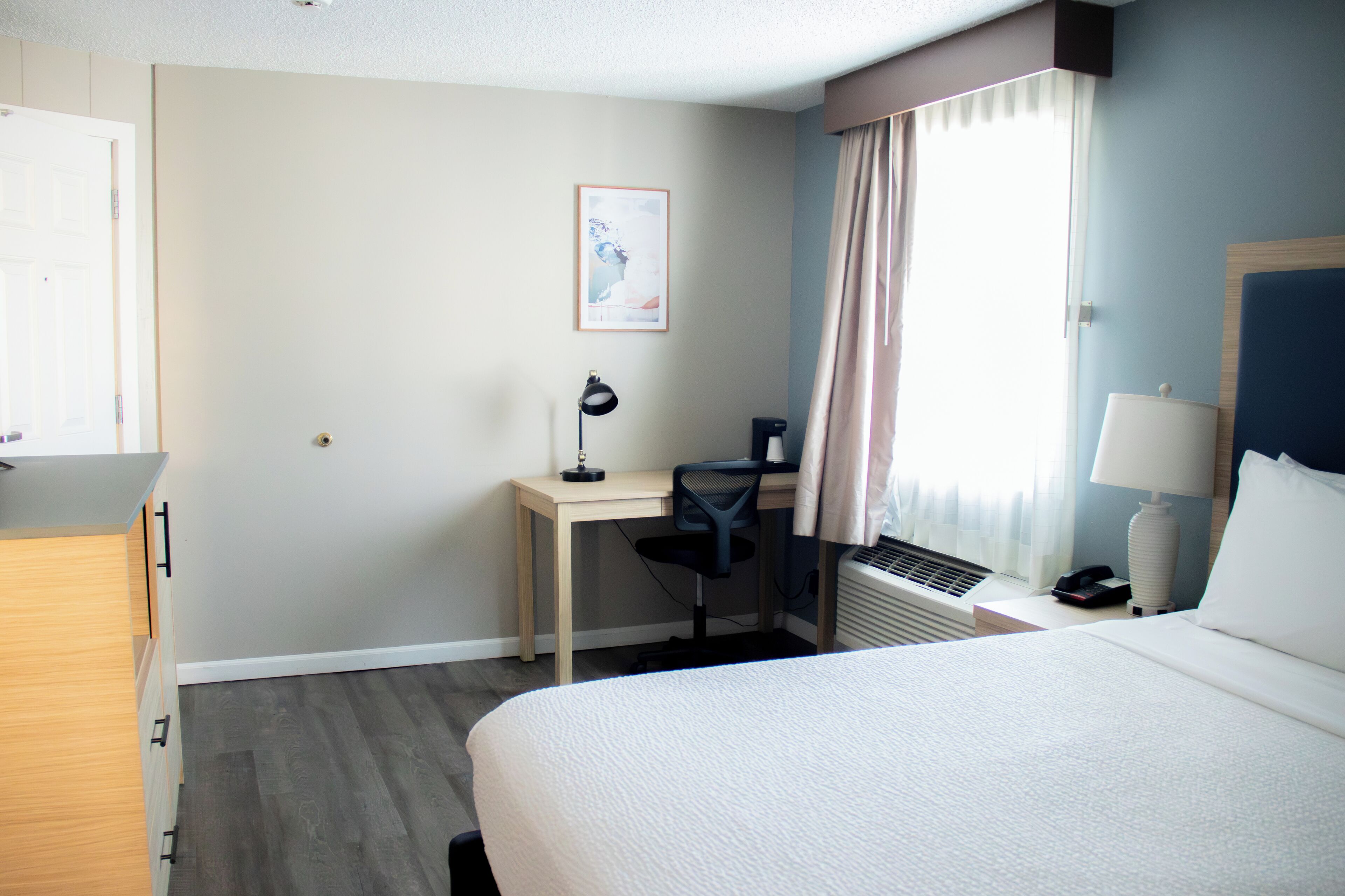 Habitación de hotel con cama, escritorio, silla y ventana con cortinas.
