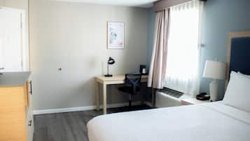 Habitación de hotel con cama, escritorio, silla y ventana con cortinas.