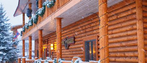 A log cabin with a porch decorated with garlands and snow-covered benches.