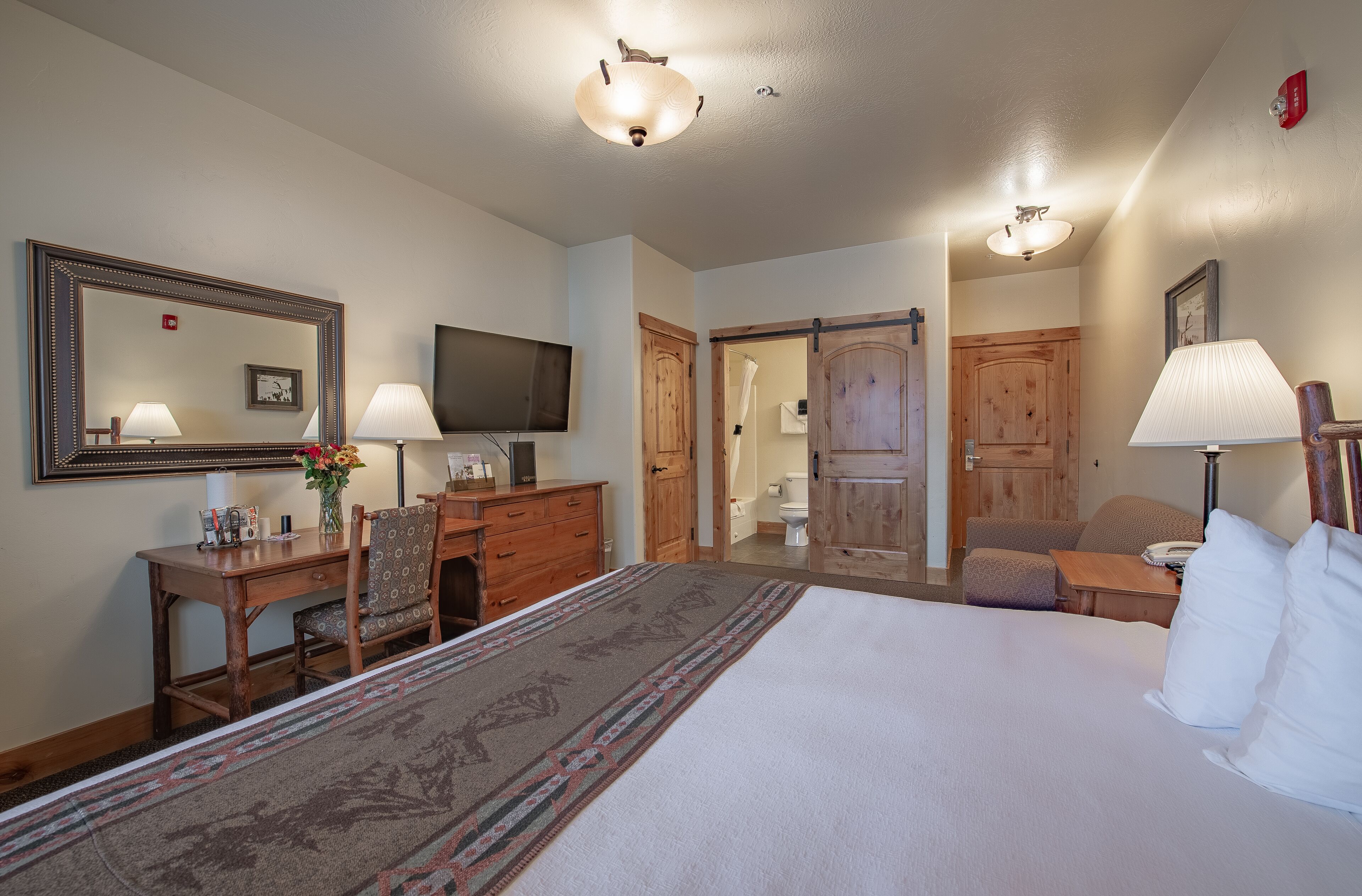 A hotel room with a large bed, a desk with a chair, a television, and a bathroom visible through an open door.