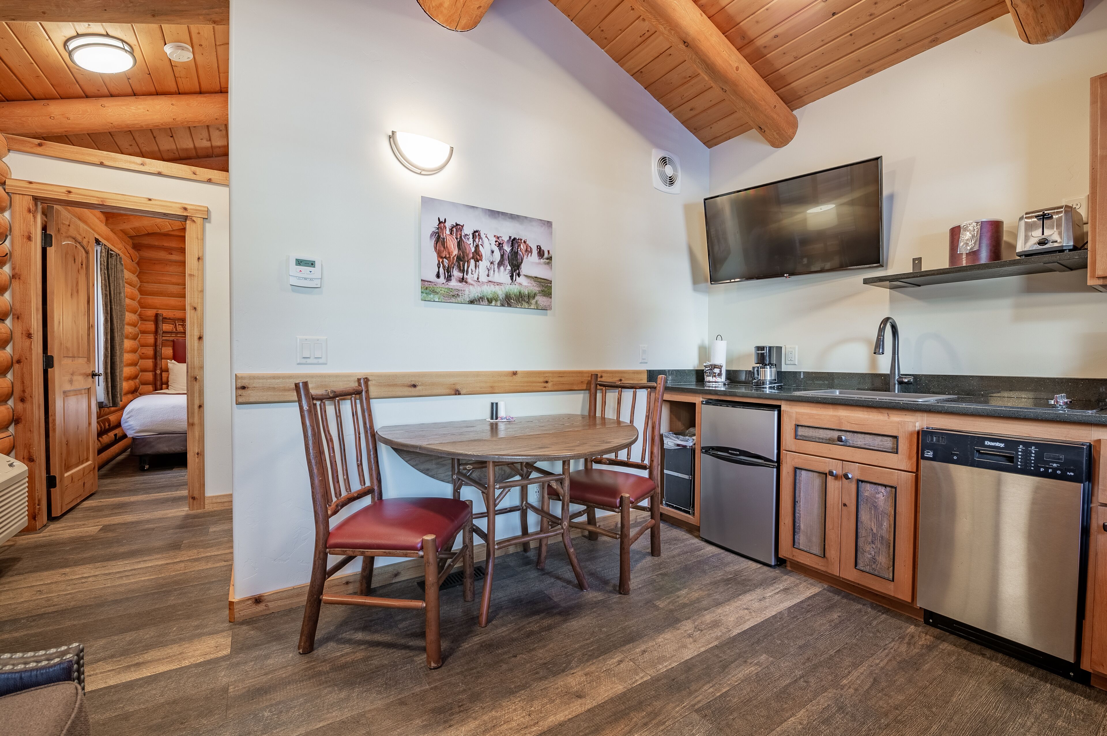 A wooden interior with a dining table and chairs, a kitchen with modern appliances, and a mounted TV.