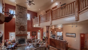 A spacious lobby with a stone fireplace, leather furniture, a wooden staircase, and a mounted elk head. - Cowboy Village Resort (Jackson)