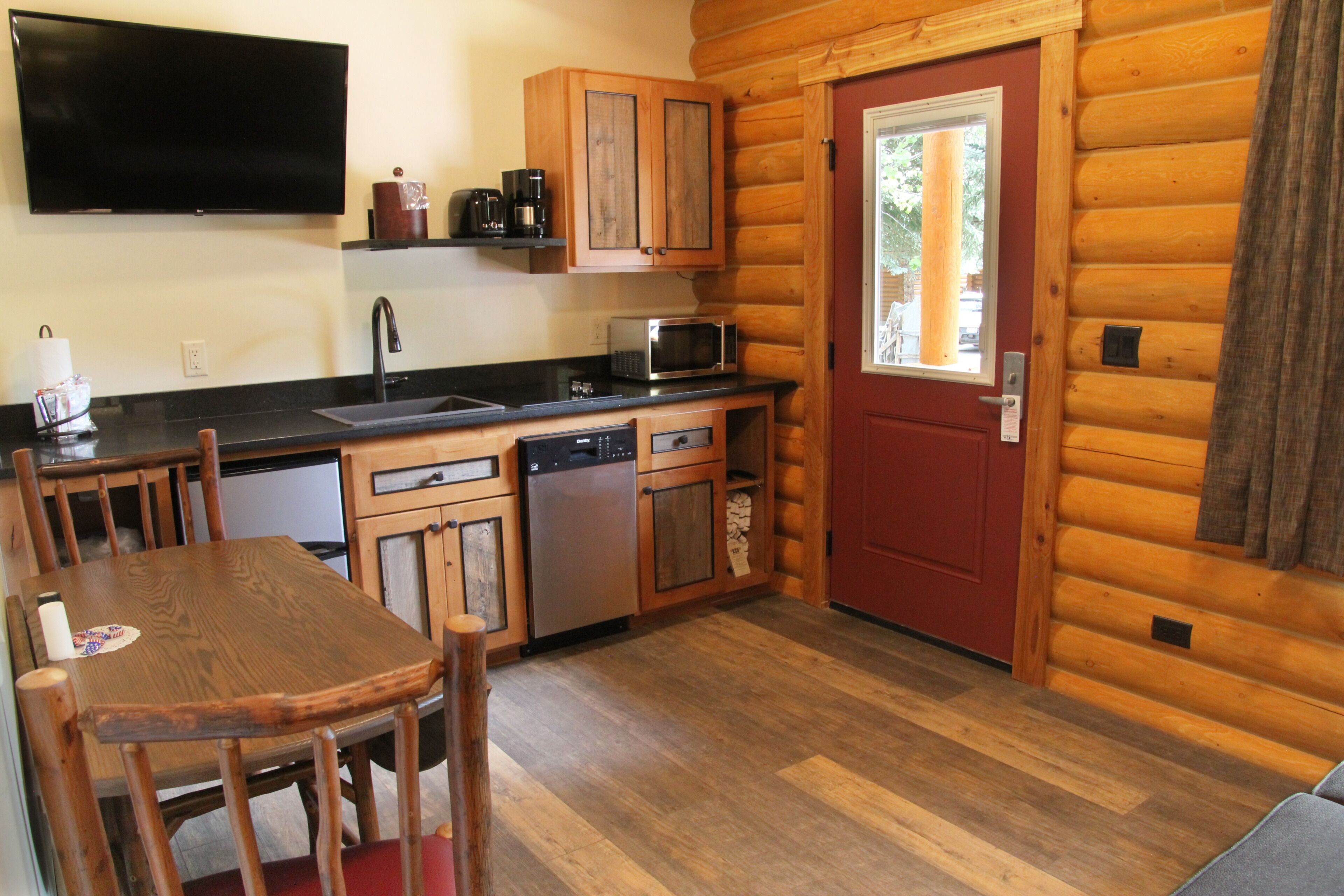A compact kitchen with wooden cabinets, a microwave, a dishwasher, and a red door.