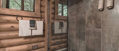 Un baño de cabaña de madera con mampara de vidrio, paredes de madera y dos dispensadores de toallas montados en la pared.