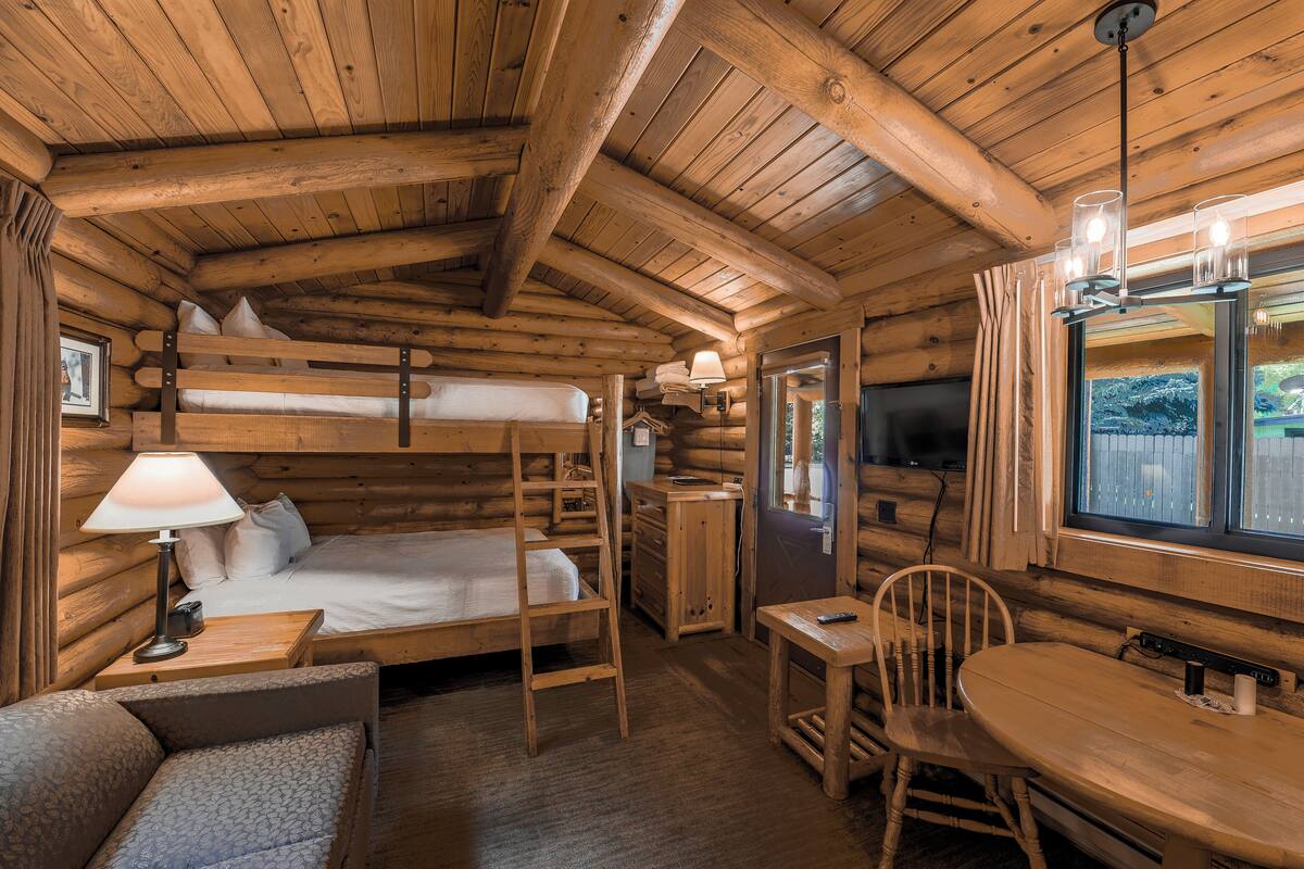 Una stanza accogliente in legno con un letto a castello, una scrivania con una sedia, un tavolino e una finestra con vista sull'esterno.