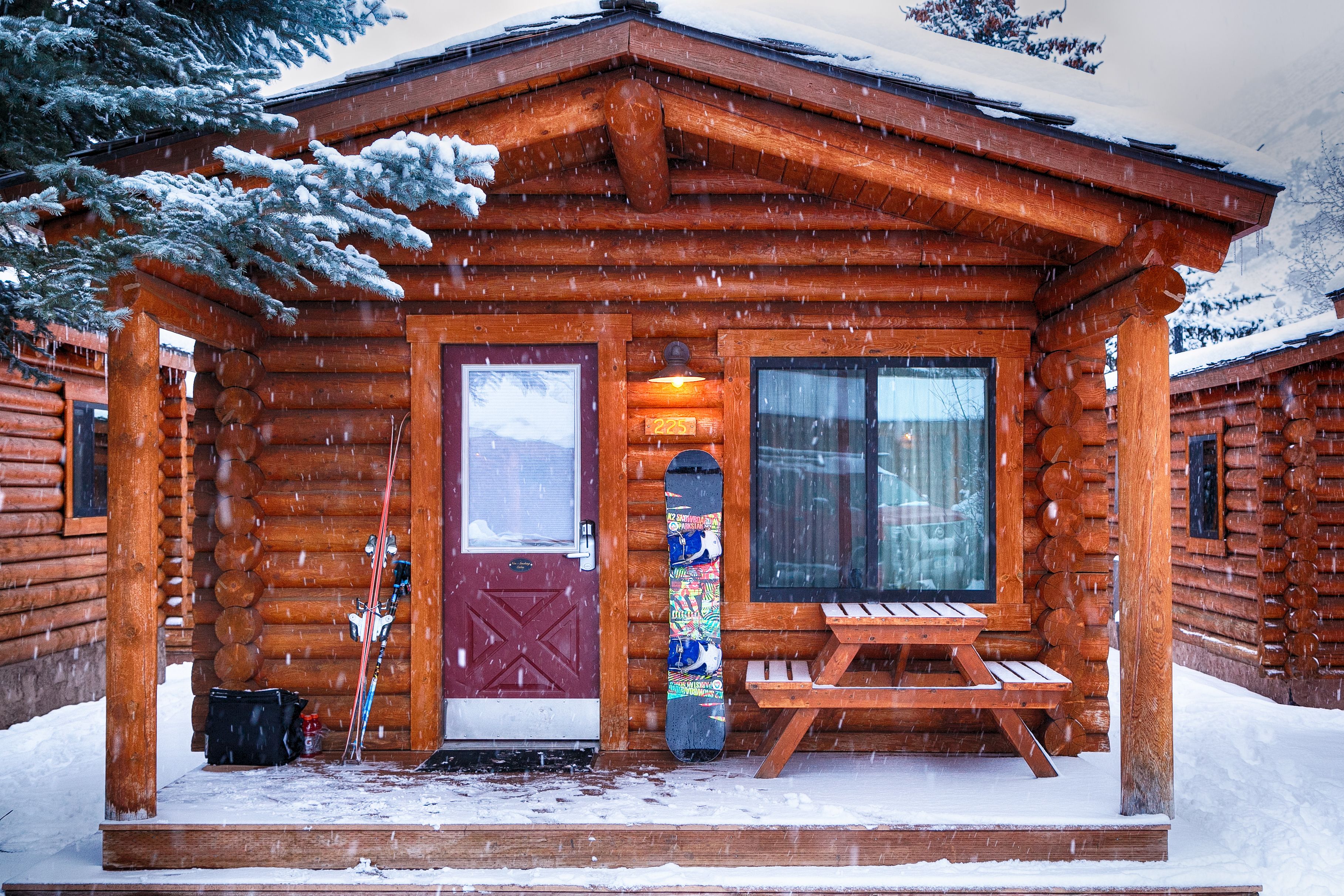 A wooden cabin with a red door, a bench outside, and snow on the ground.