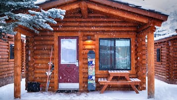 A wooden cabin with a red door, a bench outside, and snow on the ground.