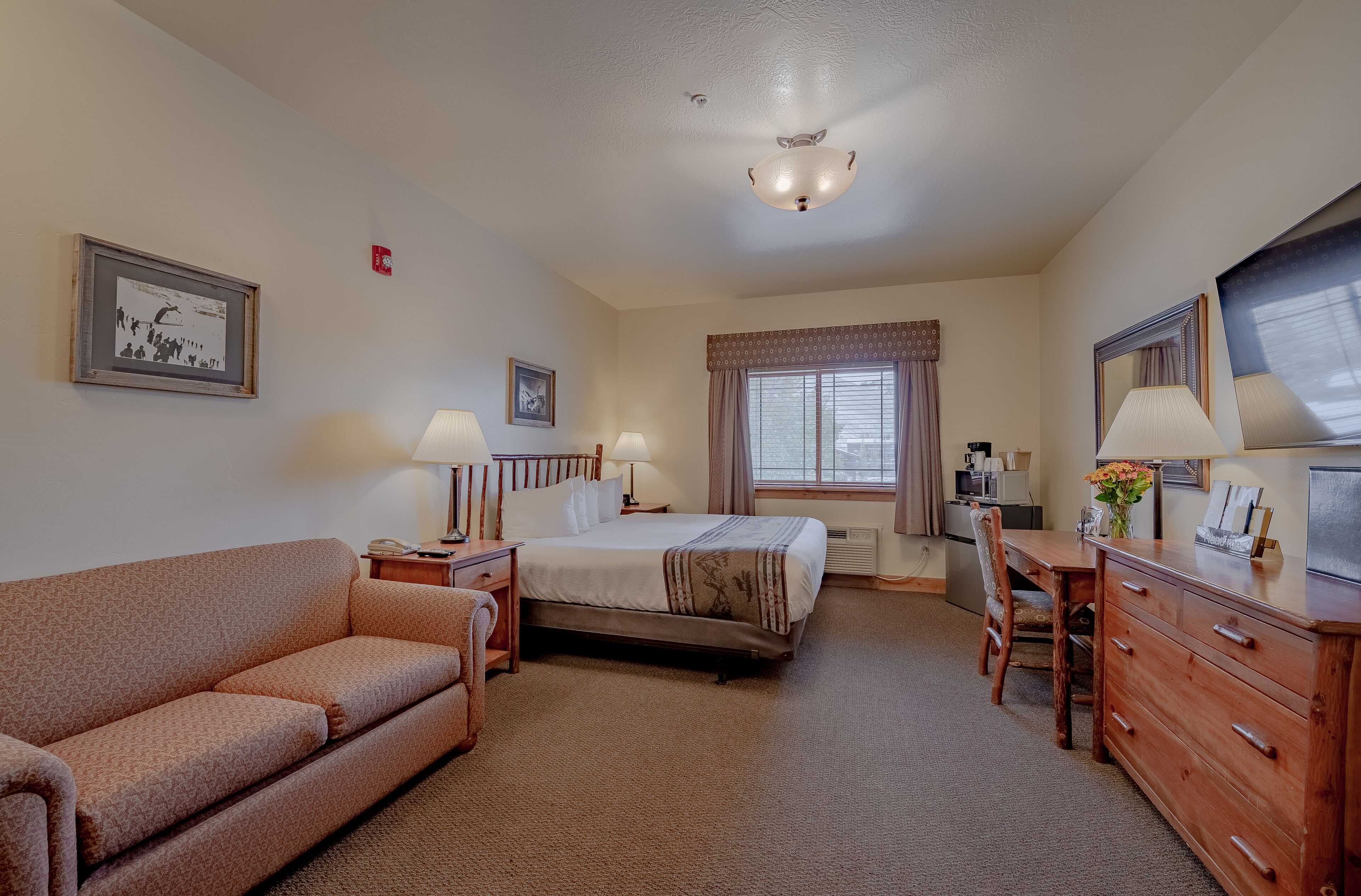 A hotel room with a double bed, a sofa, a desk, and a dresser.
