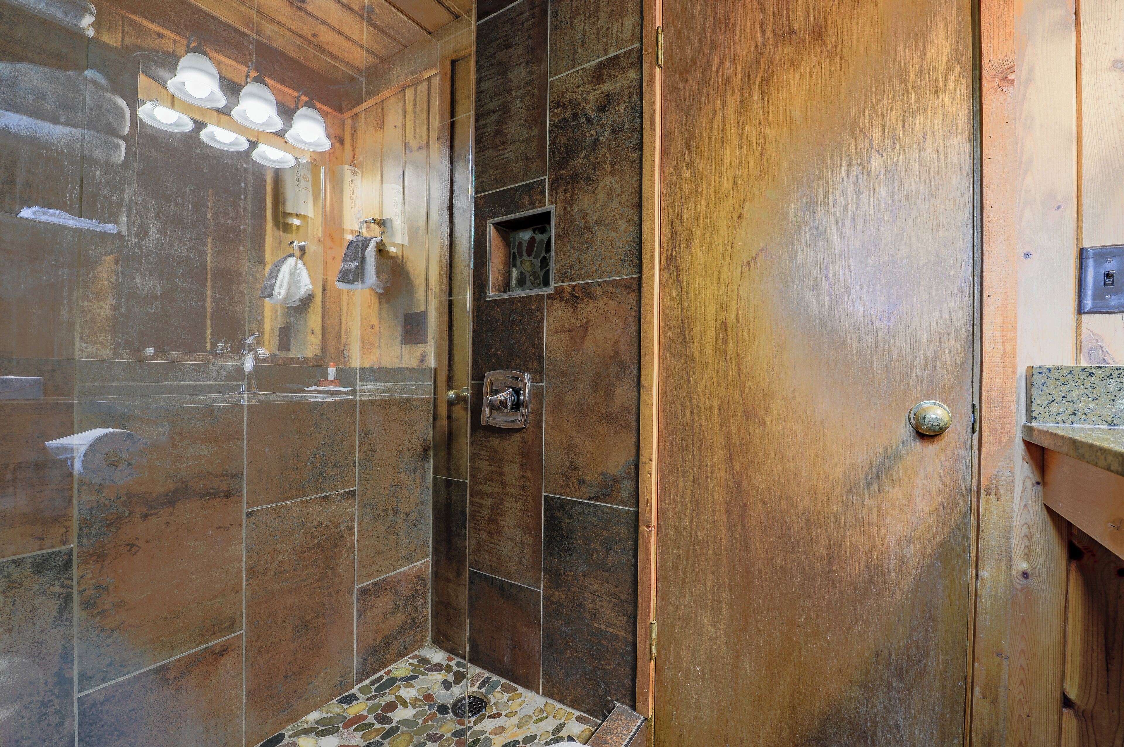 A shower with a glass door, wooden paneling, and a tiled floor.