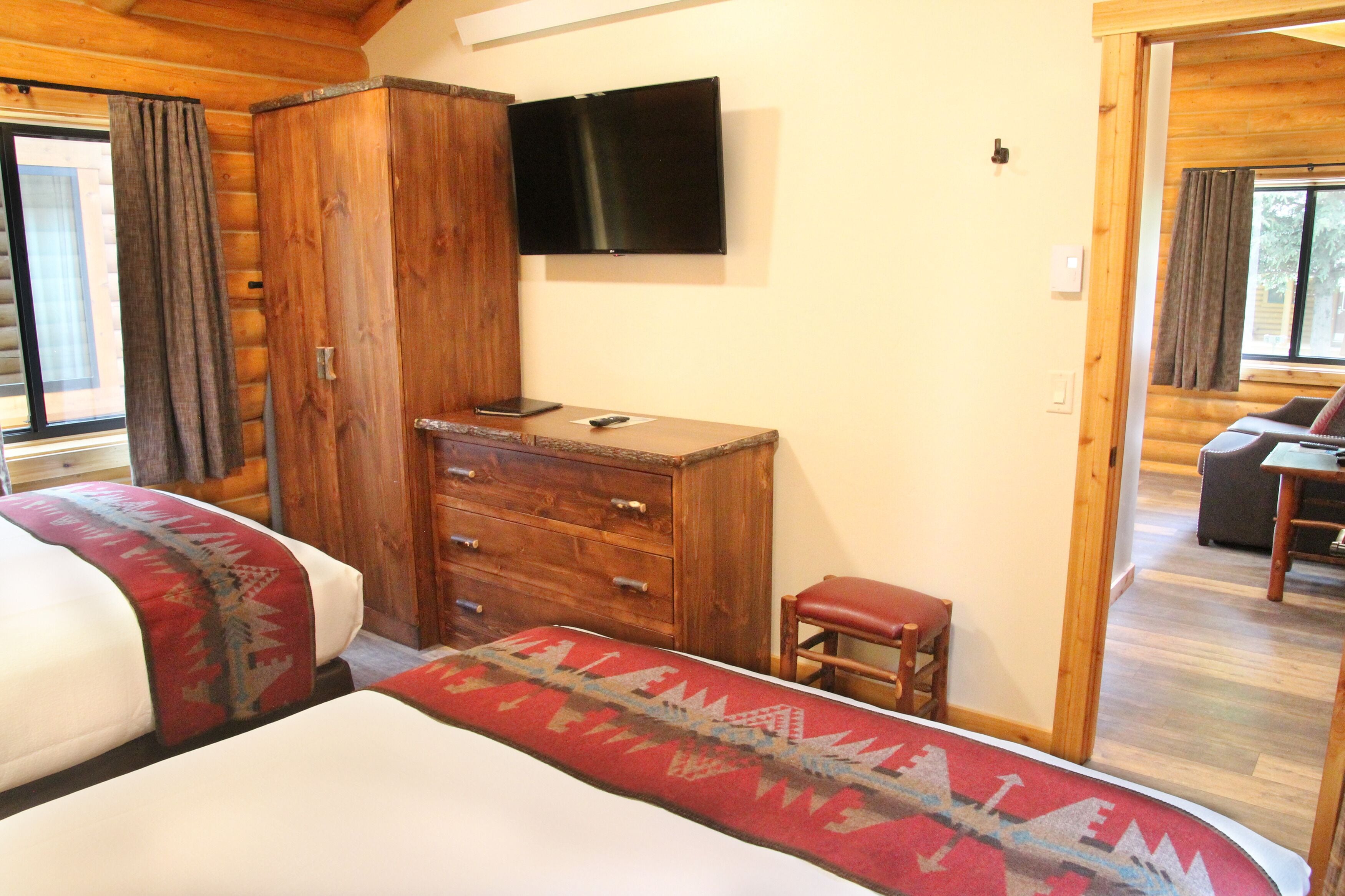 Une chambre avec deux lits, une commode en bois, un téléviseur et une petite table avec une chaise.