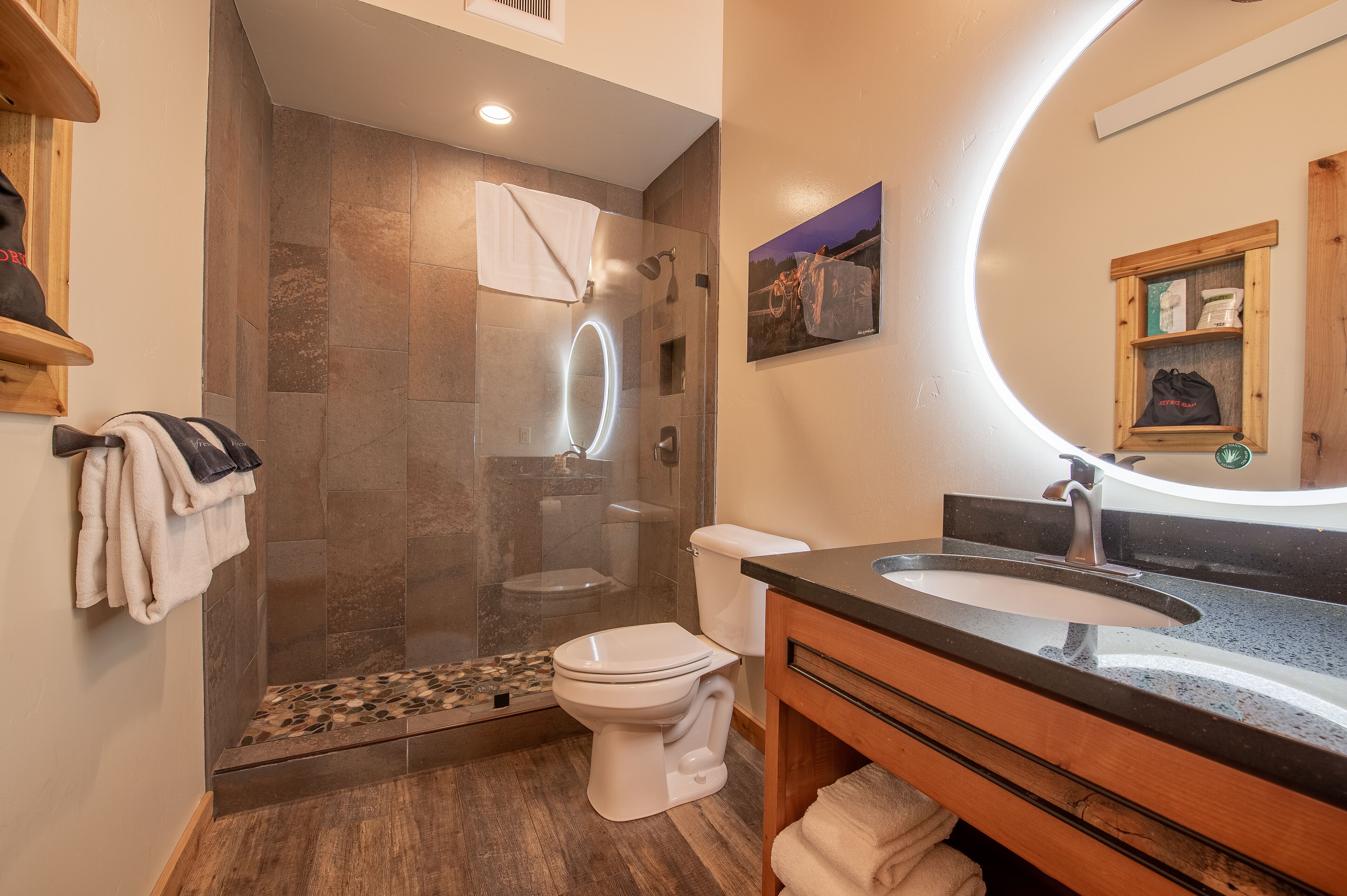 Un baño moderno con ducha de vidrio, inodoro blanco y tocador de madera con lavamanos.