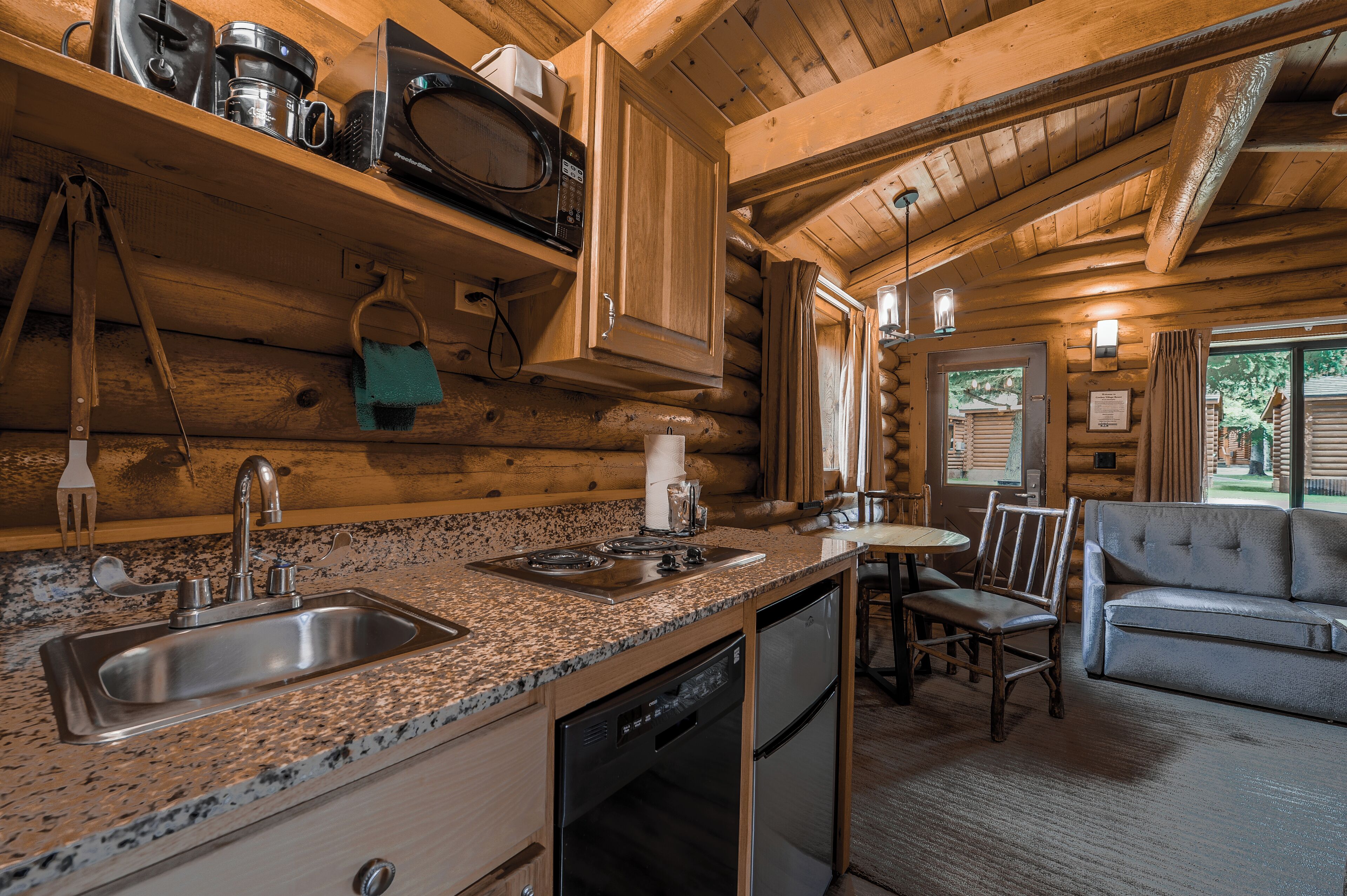 A log cabin interior with a granite countertop sink, stainless steel appliances, a dining area with a table and chairs, and a sofa.