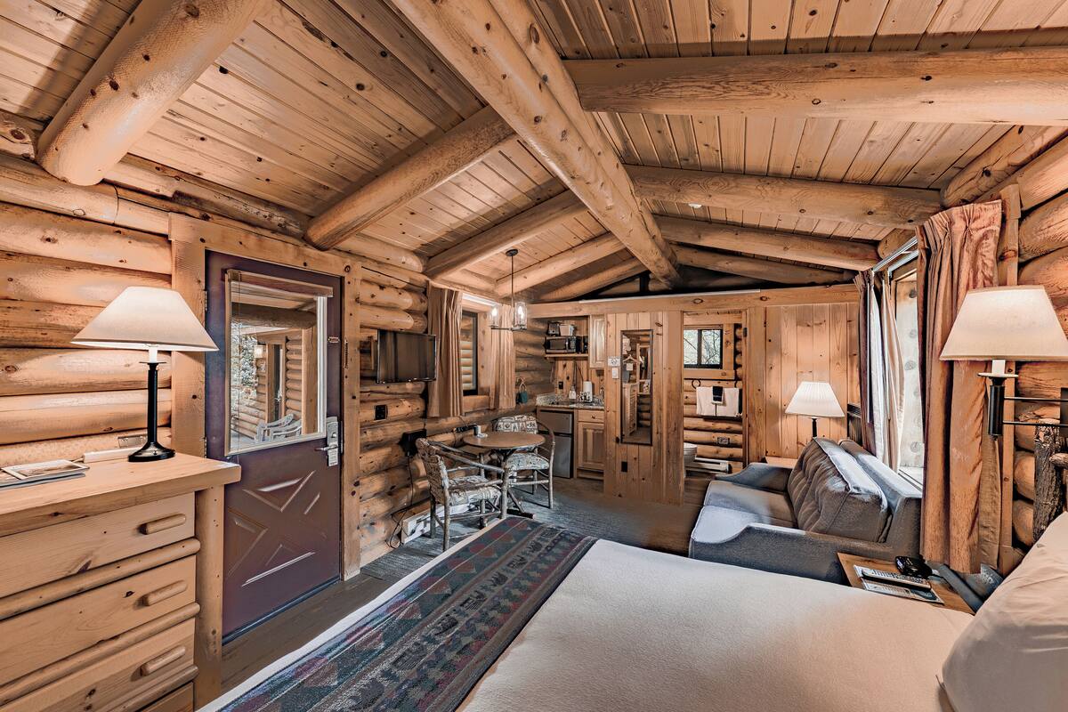 Interno di una baita di legno con un letto accogliente, un'area pranzo e una cucina.