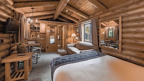 A log cabin interior with a large bed, a dining table, a sofa, and a kitchen area. - Cowboy Village Resort (Jackson)