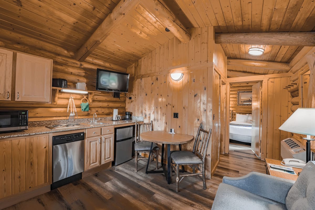 Interno di una baita di legno con cucina, zona pranzo e camera da letto.