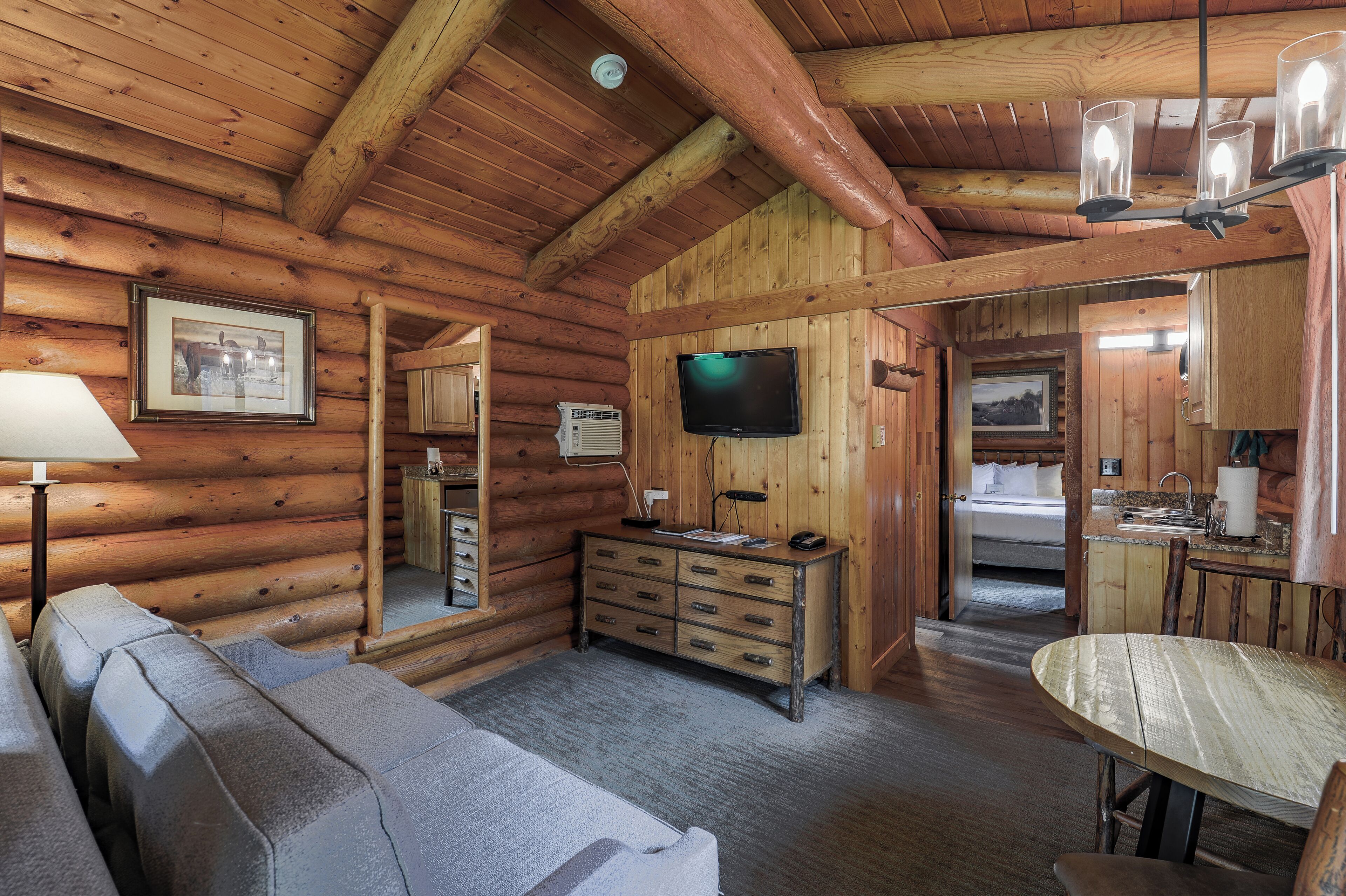 A log cabin interior with a sofa, a wooden dresser, a television, and a dining table.