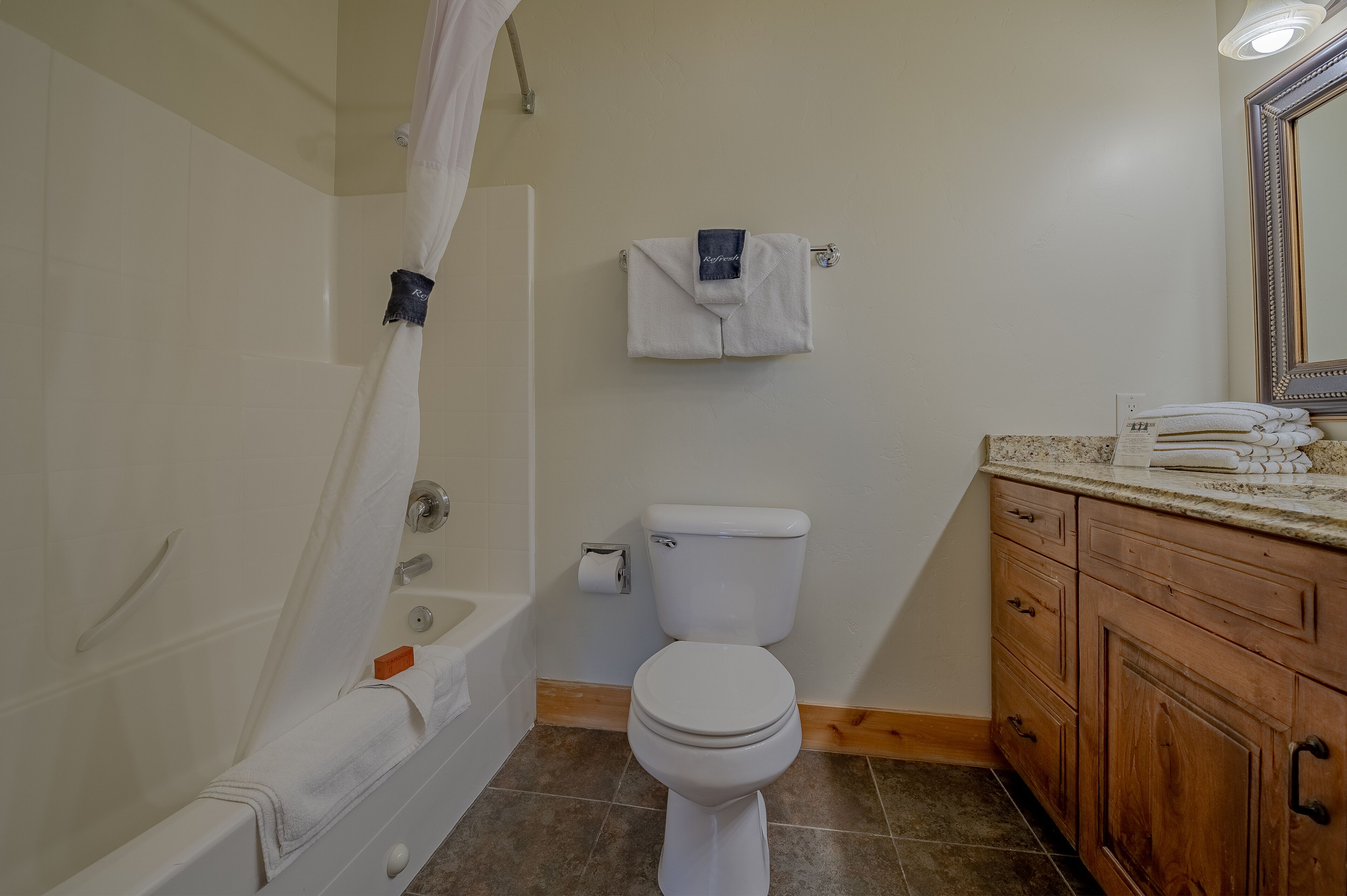 Un baño con bañera, inodoro y tocador de madera con cajones.