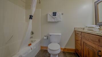Un baño con bañera, inodoro y tocador de madera con cajones.