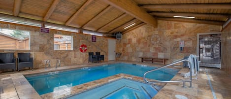 An indoor swimming pool with a wooden ceiling, stone walls, and a lifeguard chair.