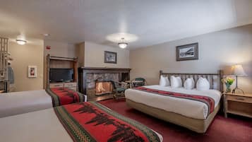 A hotel room with two beds, a fireplace, a television, and a nightstand with a lamp.