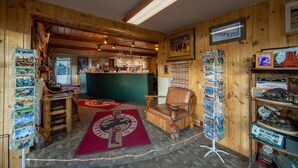 Un interior de madera con una mesa de recepción, una zona de bar y una exhibición de postales y fauna local.