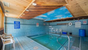 Una piscina con techo de madera y paredes de azulejos, equipada con sillas de socorrista y un flotador.