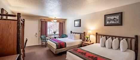 Habitación de hotel con dos camas, cabecero de madera, una mesita con una silla, ventana con cortinas y un cuadro en la pared.
