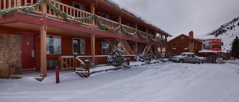 A two-story lodge with a red exterior, a balcony with Christmas decorations, and a sign for the Antler Motel Office.